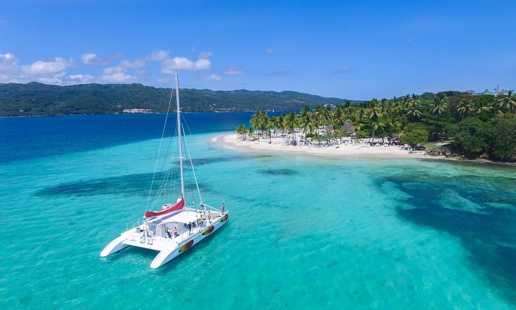 Catamarán de vela blanco en aguas turquesa frente a Cayo Levantado